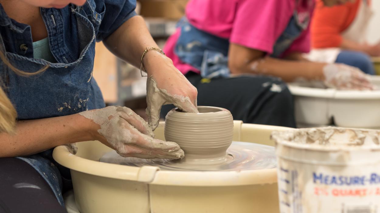 A woman works on a clay pot on a wheel in the BCA clay studio.