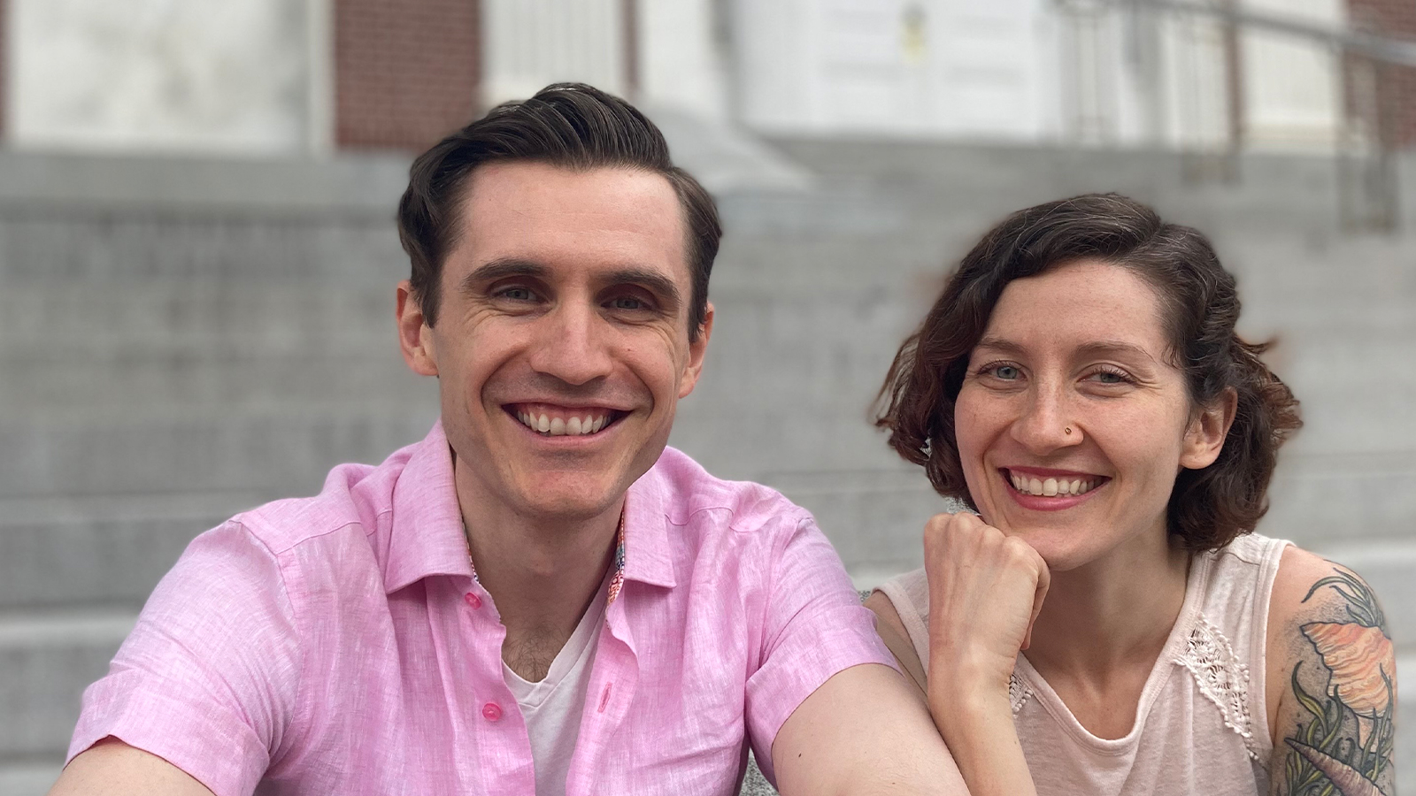Quinn Rol and Gina Stevenson look and smile at the camera from the steps of City Hall