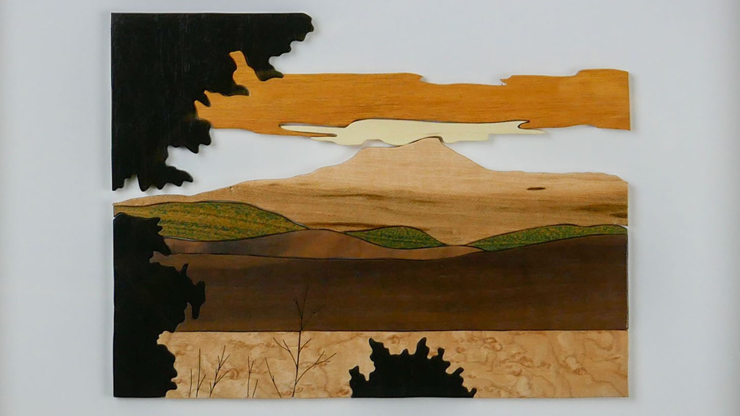 cut wood of different shades of brown forming an image of a meadow with Camel's Hump mountain in the background and clouds overhead.