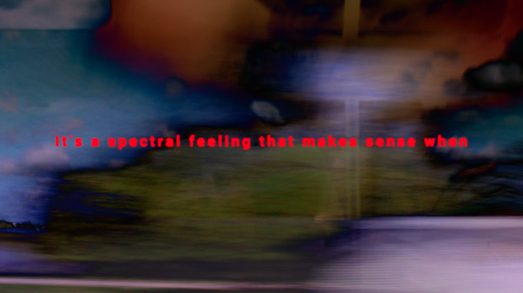 a still from a film that shows a blurred background of olive green, purple, blue and brown, with the words in red &quot;it's a spectral feeling that makes sense when&quot;