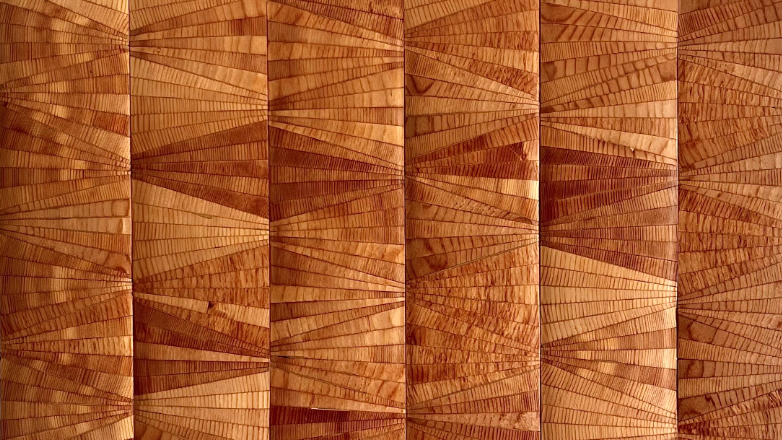 A photograph of a geometric wood panel formed by strips of wood of varying shades of gold and brown 