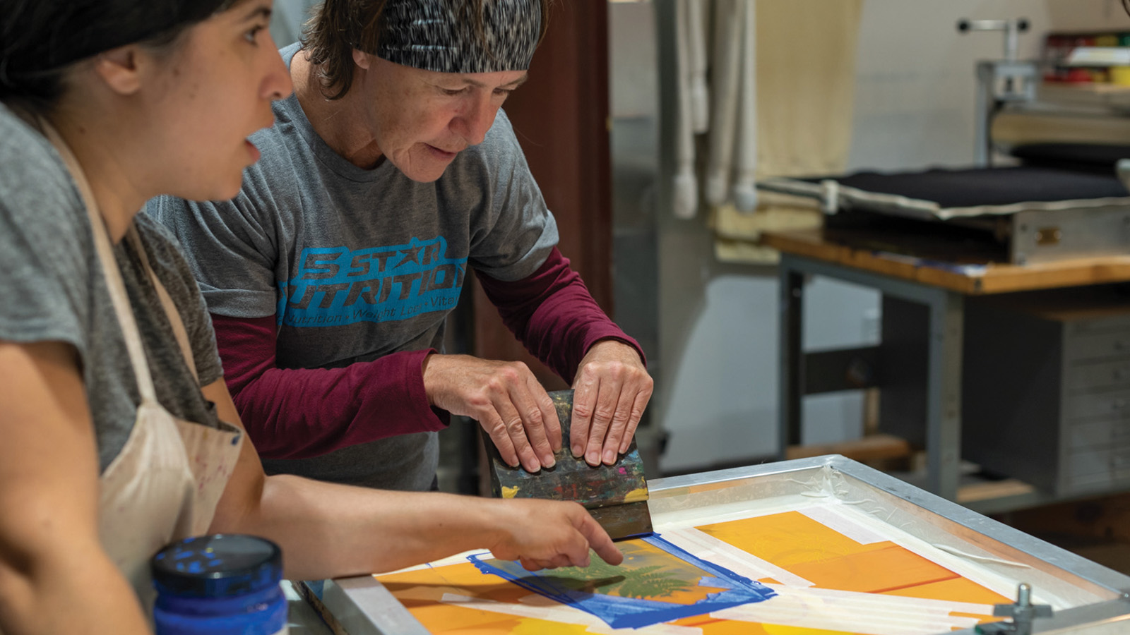 an adult getting instruction while pulling ink through her screen