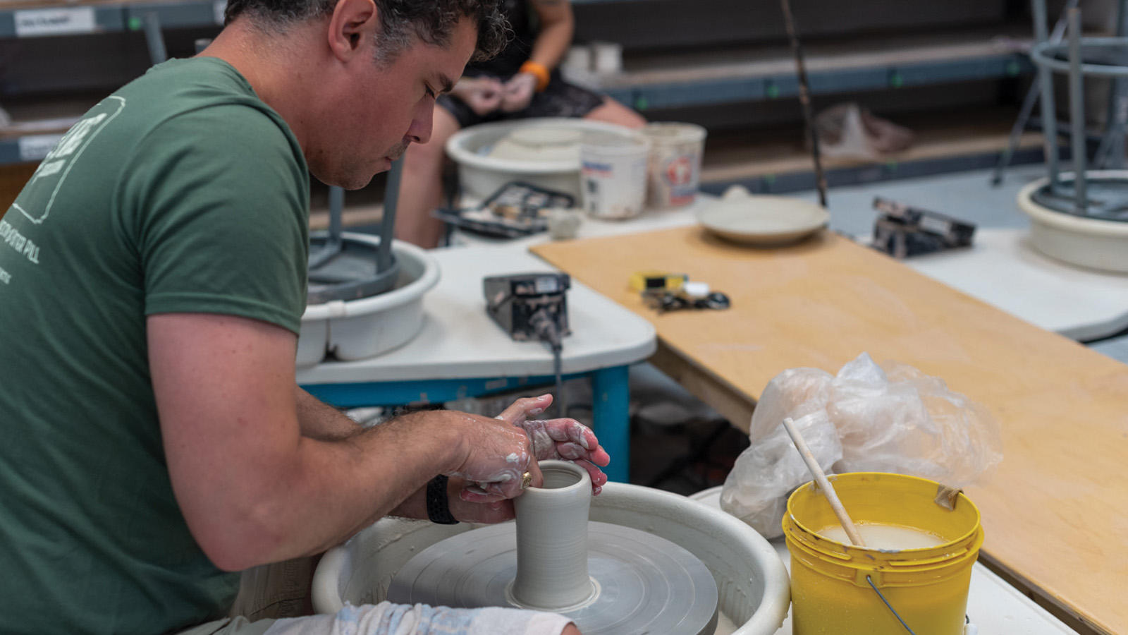 an adult at the potters wheel making a mug