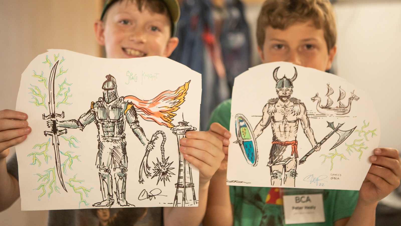 two youth displaying their drawings of fantasy characters