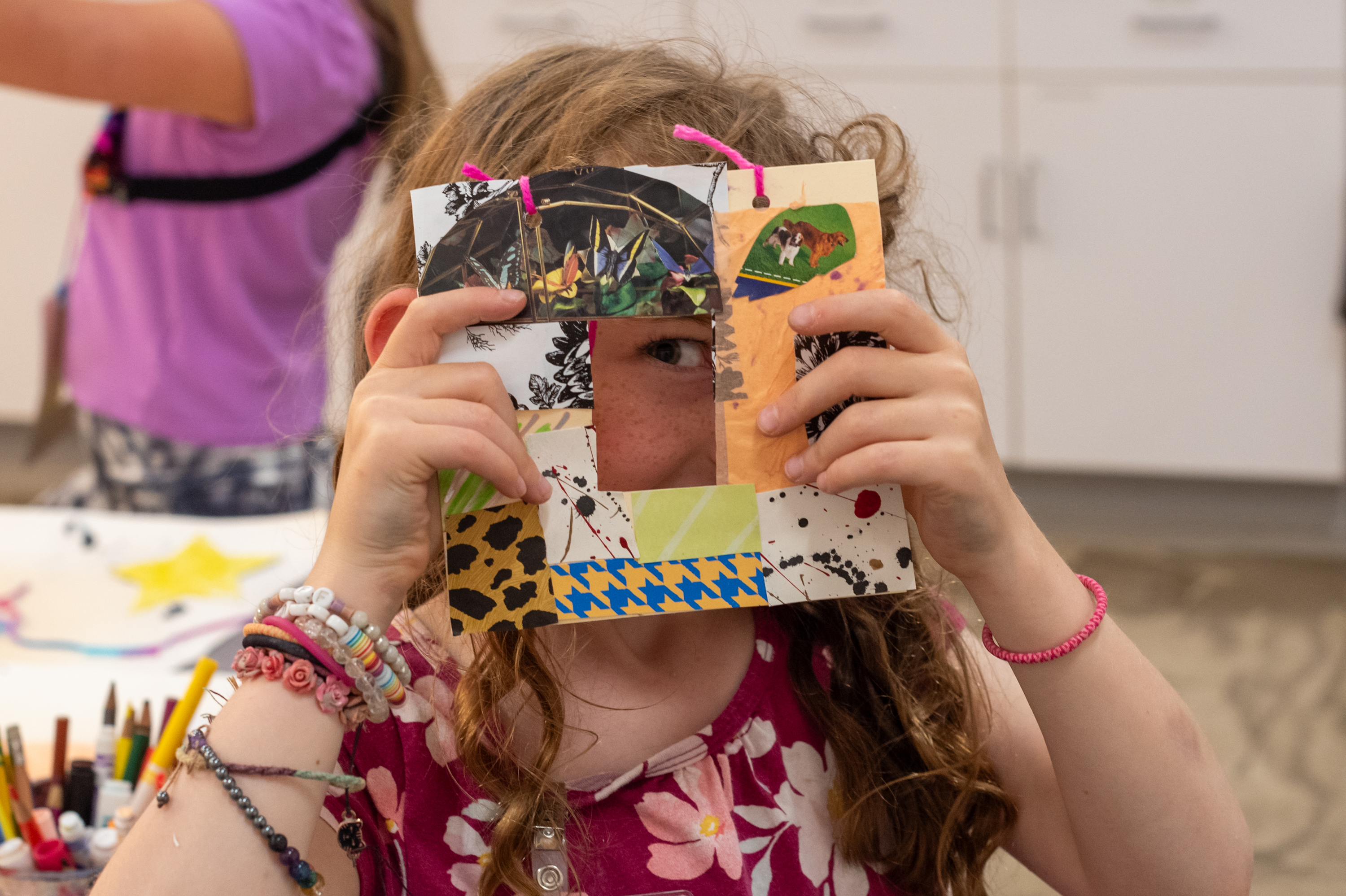 Child holding piece of art over the.ir face with their eye peeking through