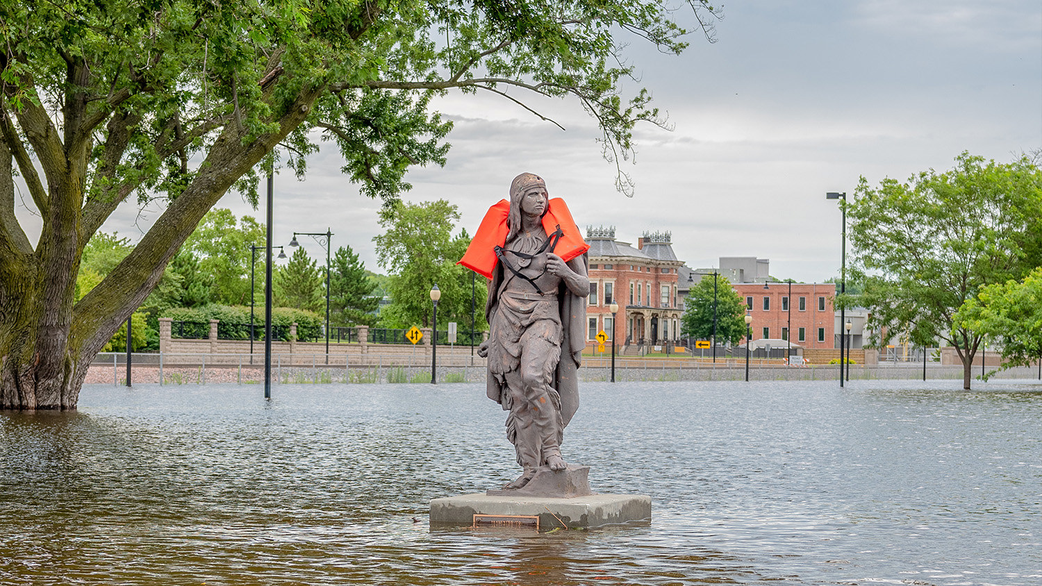 A photograph of a statue wearing a life jacket on a flooded street