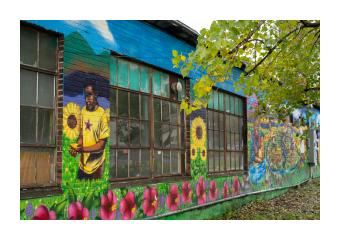 a mural depicting a black teenager wearing a yellow tee shirt, standing in a colorful field of sunflowers