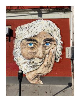 a mural of the head of an older man with light skin and white hair and a beard, resting his head on his chin