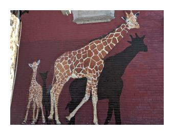a mural of a mother and baby giraffe painted on a red brick wall, with their shadows painted behind them