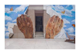 a trompe l'oeil mural of two hands ripping a blue sky dotted with clouds and butterflies apart over a doorway 