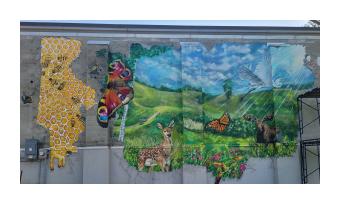 a mural of a green meadow with deer, butterflies and swirling blue skies above