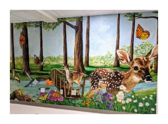a mural of fawns standing in a meadow with a bridge that stretches across a small brook with trees and monarch butterflies in the background