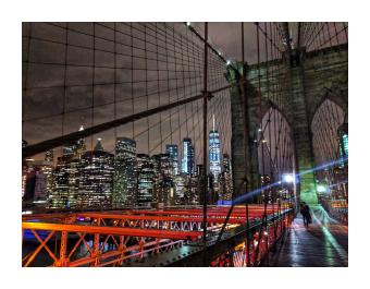 A photograph of the brooklyn bridge at night up close with an illuminated New York City skyline 