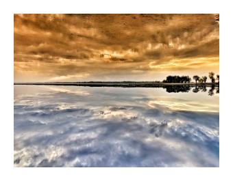 A photograph of a bronze cloudy sky reflected in a blue lake.