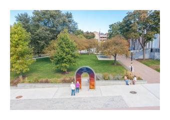A couple stands in the middle of a city park in front of an acrylic and colorful art installation.