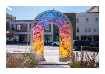 Close up of an acrylic and colorful art installation at the edge of a park facing city buildings.