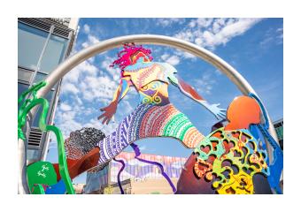A photo of Dance in Place an outdoor public sculpture in Burlington, VT that consists of colorful intertwined steel cutouts of people dancing within a suspended steel ring 
