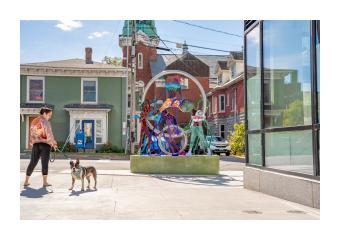 A photo of Dance in Place an outdoor public sculpture in Burlington, VT that consists of colorful intertwined steel cutouts of people dancing within a suspended steel ring 