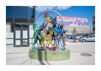 A photo of Dance in Place an outdoor public sculpture in Burlington, VT that consists of colorful intertwined steel cutouts of people dancing within a suspended steel ring