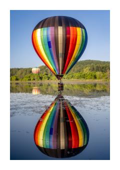 photograph of colorful hot air balloon on lake surface with reflection