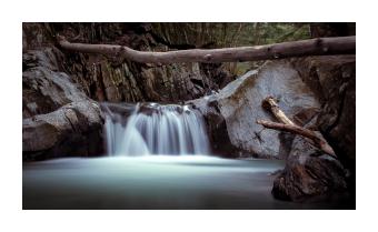 Photograph of a waterfall taken at eye level where the waterfall is a soft blue, appearing to glow, and the rocks around are blue-tinted greys. 