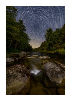 Photograph of an upriver shot at the night sky where stars circle in a spiral. 