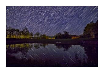Photograph of a night sky and the stars movements reflected on the lake underneath. 