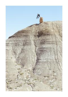 Photograph of a man jumping on a bike down a rocky cliff face. 