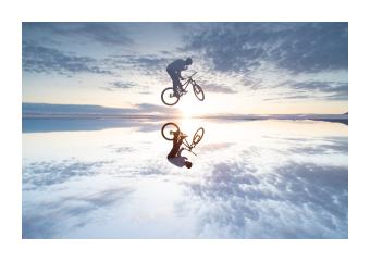 Photograph of a biker jumping a body of water where the biker is reflected in it. 