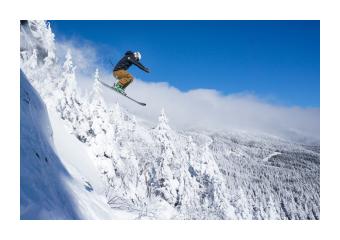 Photograph of a skier mid jump down a snowy mountainside. 