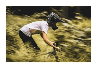 Closeup photography of a helmeted figure biking down a hill, motion blurred. 