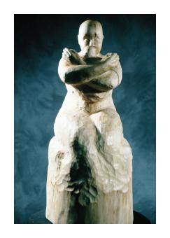 Birch sculpture depicting a figure embracing themself. 