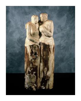 Birch sculpture of two female figures embracing -- one looks at us, the other at her partner.