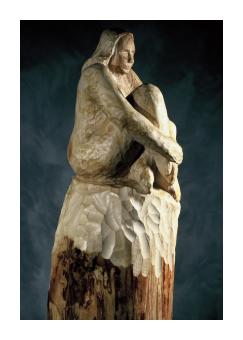 Birch wood sculpture of a woman, knees pulled up to her chin. 