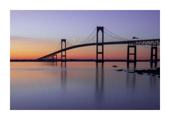 Photograph of a bridge across the water at sunset.