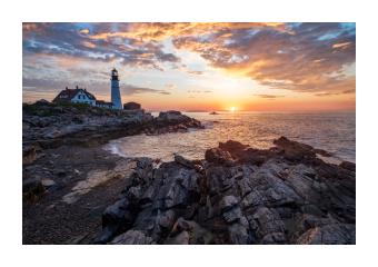 Photograph of a rocky shore on the water at sunset.