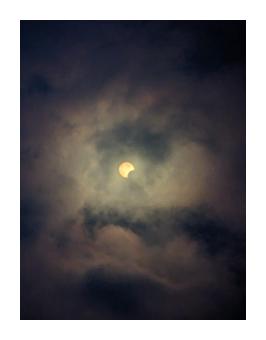 Photograph from the ground depicting the eclipse among clouds. 