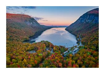 Photograph of an encased lake surrounded by autumn forests and mountains. 