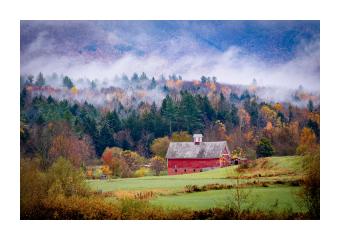 Photograph of a red barn amongst a sprawling field and forest. 