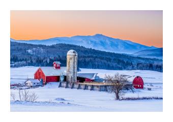 Photograph of a farm at sunrise among a snowy landscape with mountains in background. 