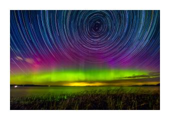 Vibrant photograph depicting the circular motions of the stars during an aurora borealis -- in lime green, purple, and deep blue. 