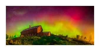 Photograph depicting a barn during aurora borealis proceedings in lime green, flourescent pink, and purple. 