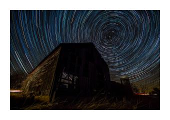 Photograph depicting the circular motions of the stars in deep blue behind a barn. 