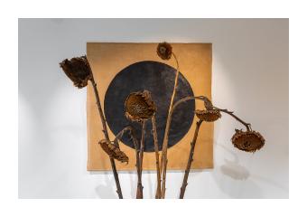 Sculpture of a series of sunflowers in a box placed in front of a canvas in orange with a black circle.