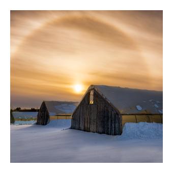 Photograph of a series of three greenhouses in the snow at sunset. 