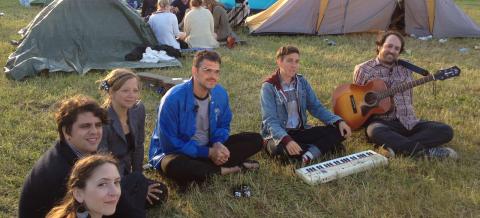 the band with instruments sitting in a field with camping tents in Finland