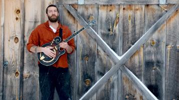 artist holding a banjo in front of wooden barn door