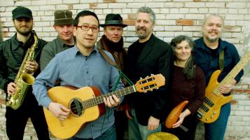 The members of GuaGua stand in front of a brick wall holding musical instruments.