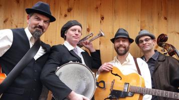 The members of Red Hot Juba stand in front of a wood paneled wall holding their instruments..