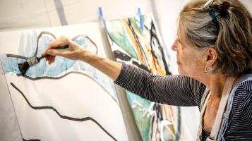 Woman painting blue paint between black lines on a canvas.